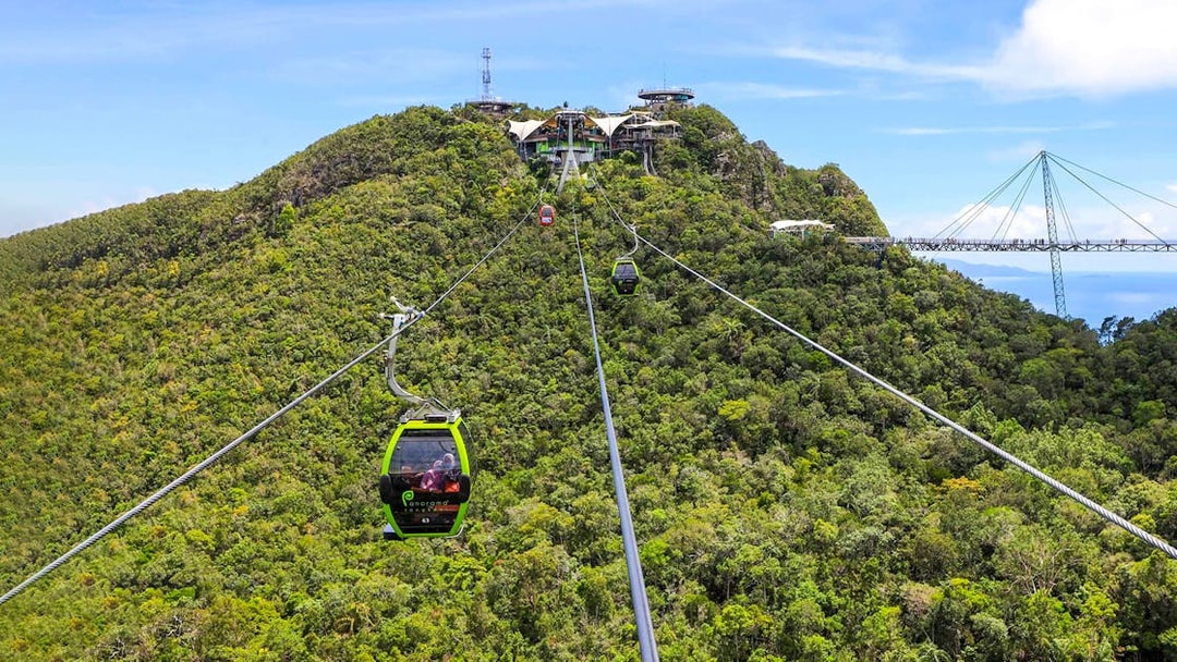 SkyCab cable car ascending over lush hills in Langkawi, with Sky Bridge in the background.