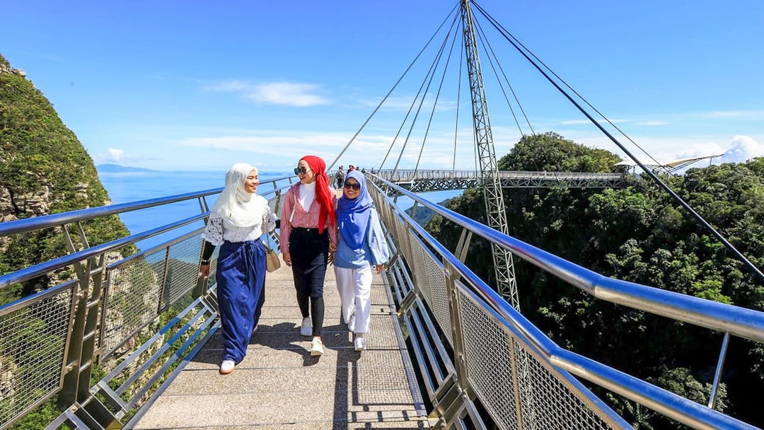 Women walking on Langkawi Sky Bridge with scenic views of the forest and ocean.