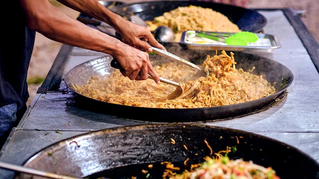 Langkawi street food vendor cooking noodles in a large pan.