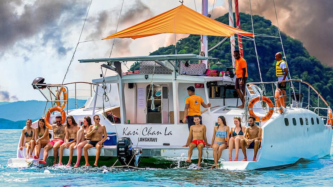 Group enjoying a sunset cruise on a catamaran in Langkawi, with lush hills in the background.