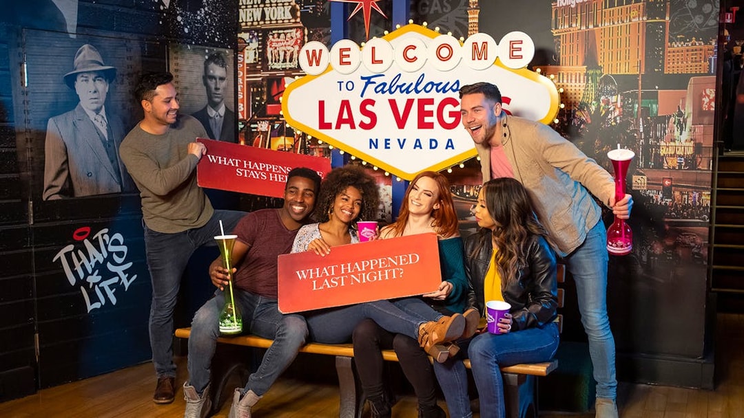 Group of friends posing with signs at the Welcome to Las Vegas sign, enjoying Go City: Las Vegas Explorer.