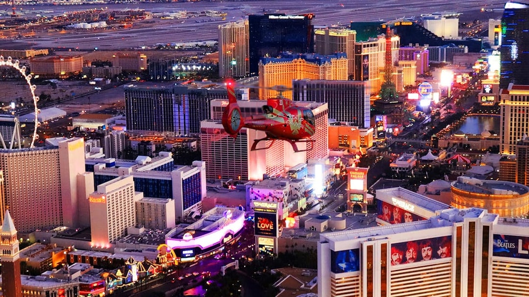 Helicopter flying over Las Vegas Strip with casinos and hotels illuminated at night.
