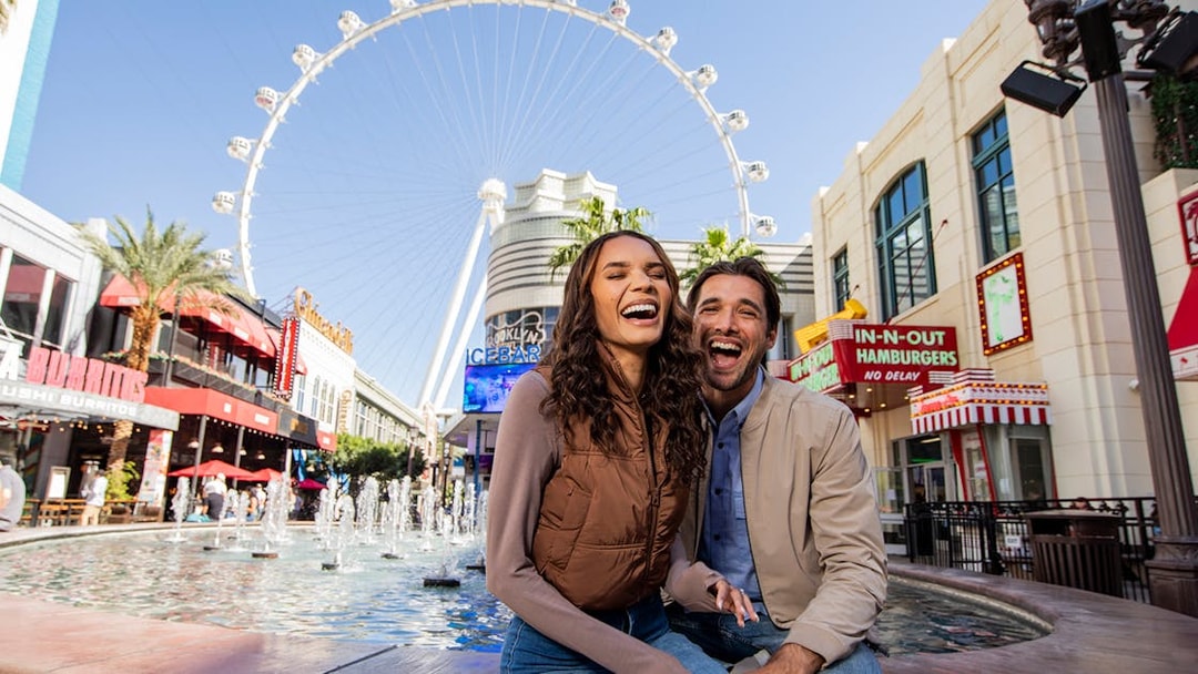 Couple smiling by fountains at The LINQ Promenade with High Roller in Las Vegas.