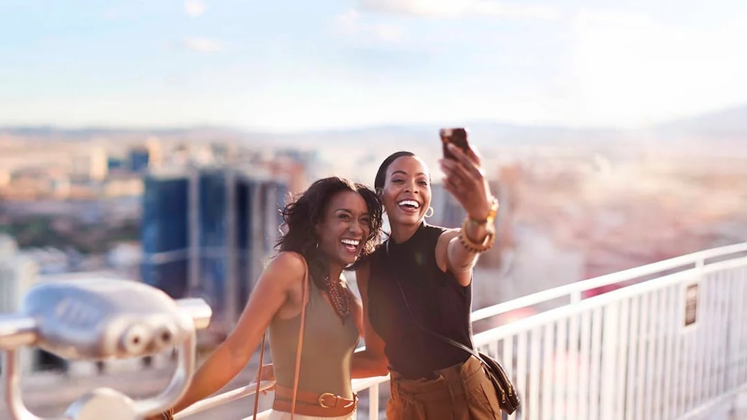 Two people taking a selfie on a Las Vegas observation deck with city view.