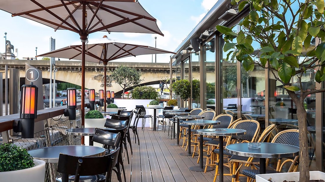 Outdoor seating at Le Bistro Parisien, Paris, with view of Seine River bridge.