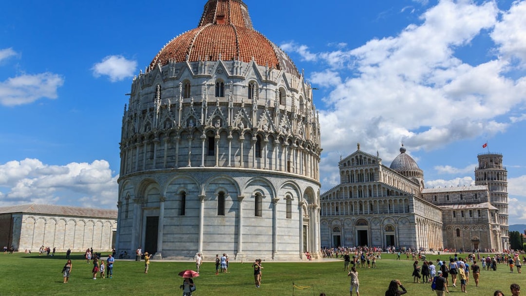 Pisa Baptistery with tourists on the lawn, Pisa, Italy.