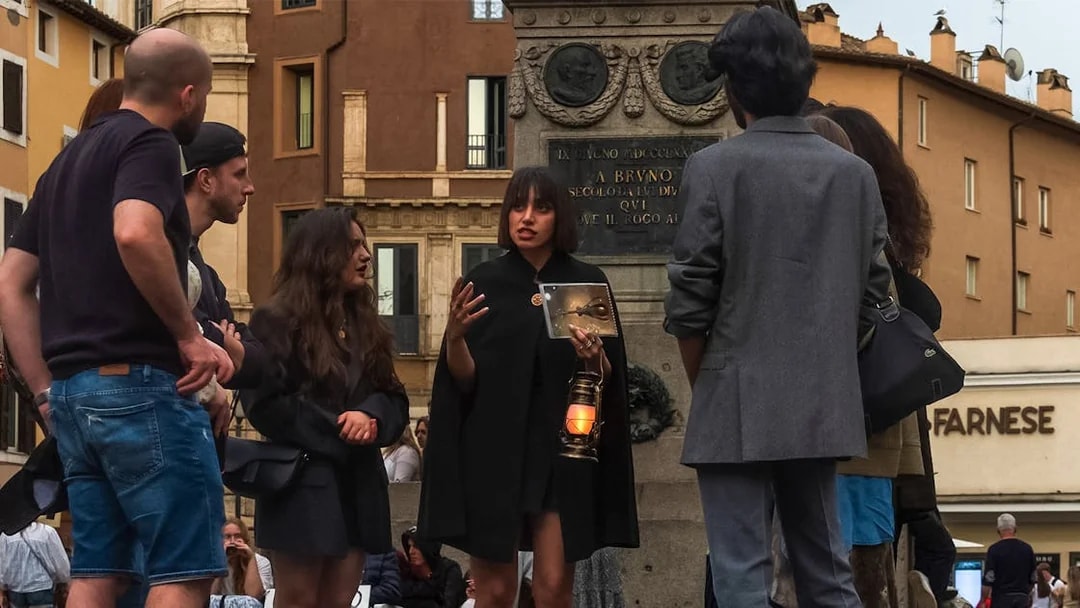 Tour guide with lantern leading tourists on legend and ghosts of Rome tour near statue.