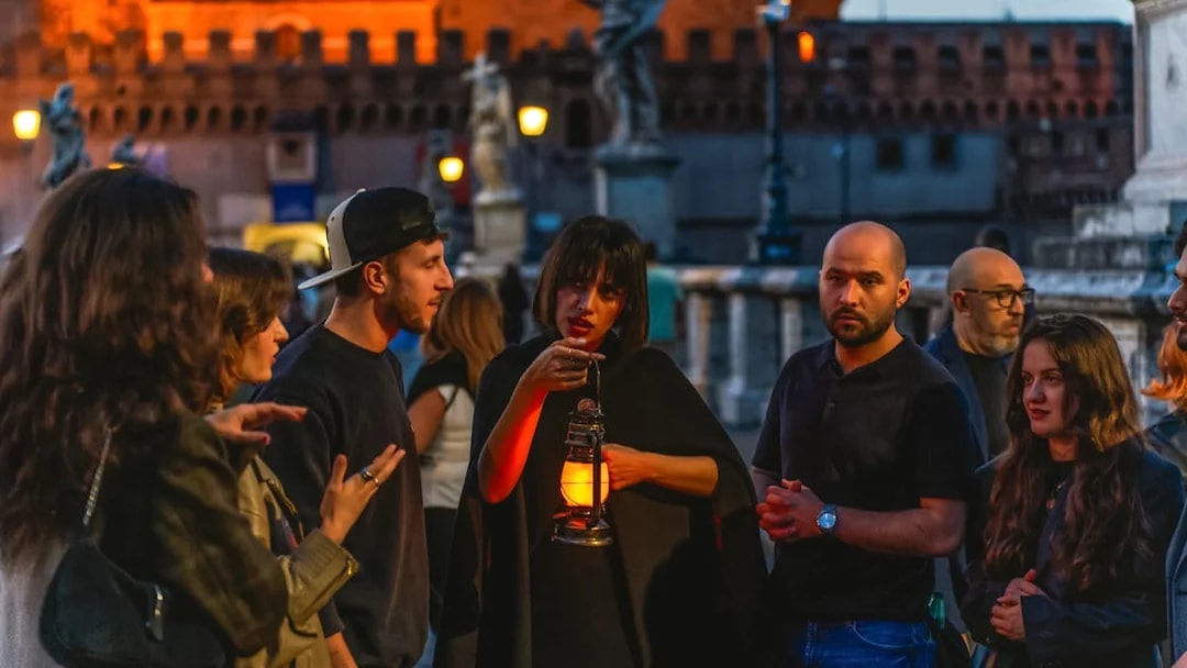 Tour guide with lantern leading tourists on Rome's legend and ghosts tour.