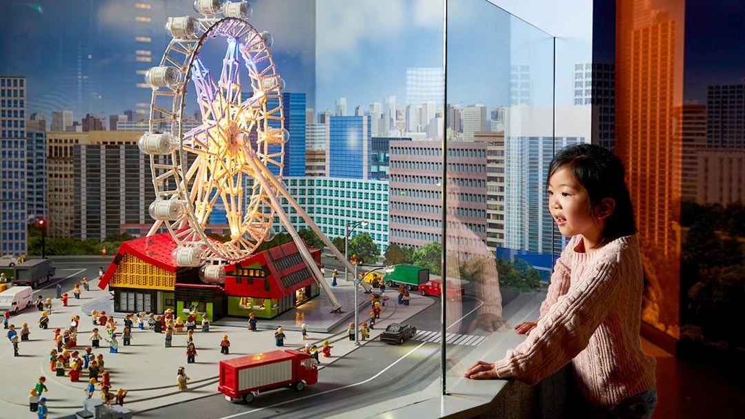 Child observing LEGO cityscape with Ferris wheel at LEGOLAND Discovery Centre.