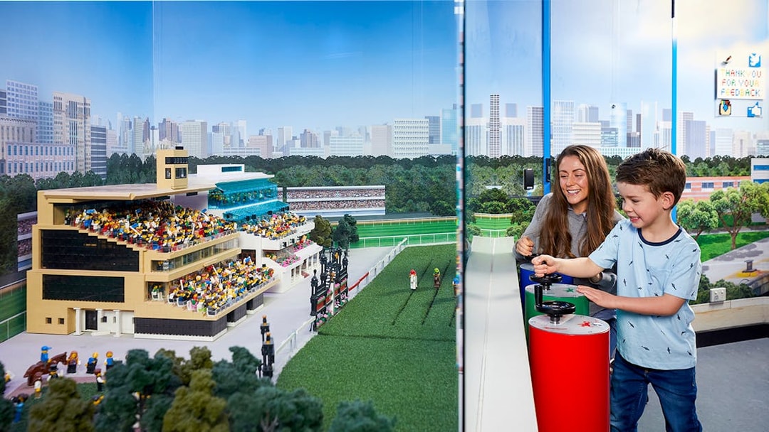 Child and adult interacting with LEGO racetrack model at LEGOLAND Discovery Centre.