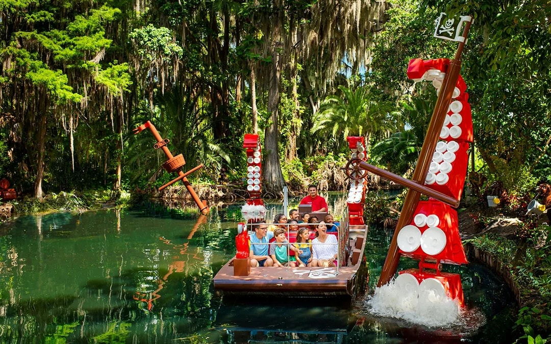 Visitors on a boat ride through a lush, pirate-themed river at Legoland Florida.