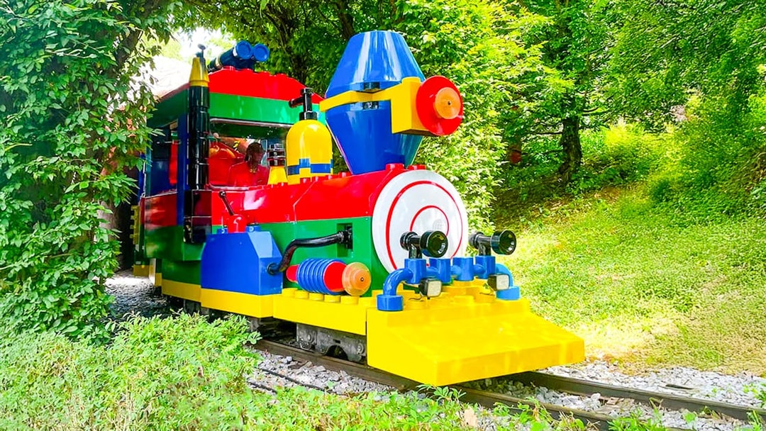 Colorful LEGO train ride at LEGOLAND Deutschland amidst greenery.