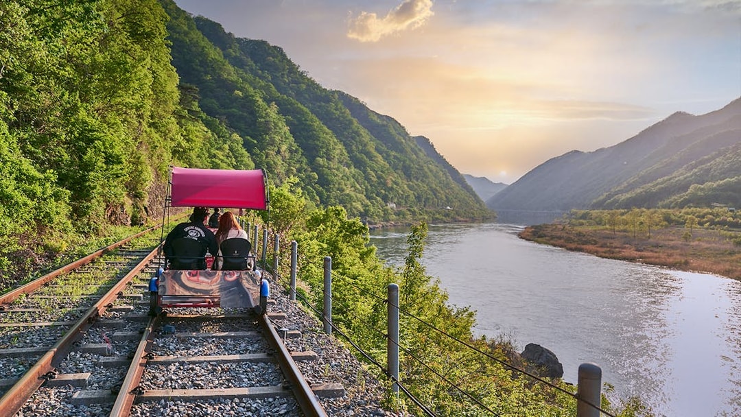 Couple riding Gangchon Railbike along scenic river and mountains at sunset in Korea.