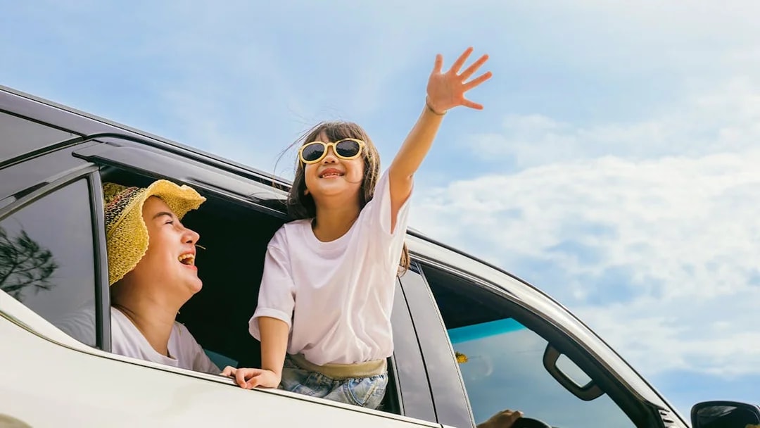 Family enjoying private car transfer with child leaning out window.