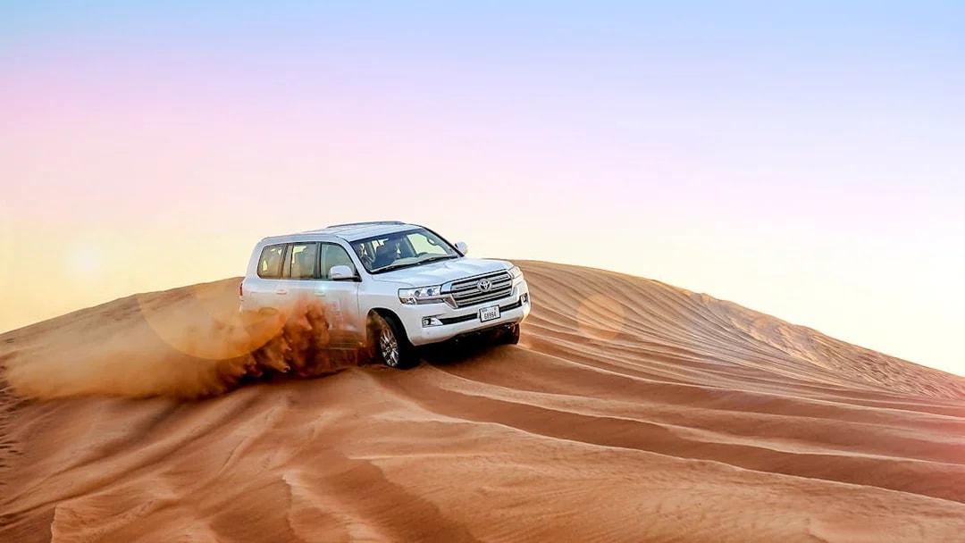 SUV driving over sand dunes during evening desert safari.