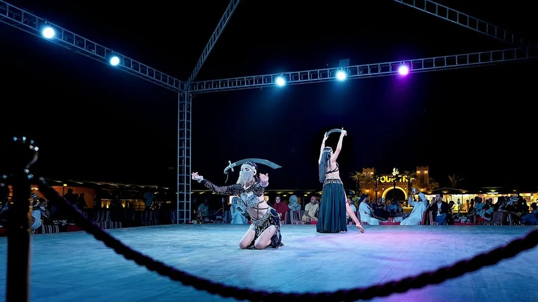 Evening desert safari performance with dancers on stage, audience watching.