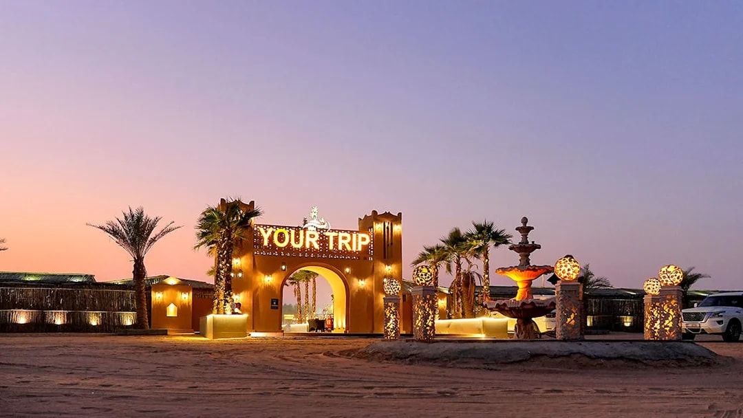 Entrance to evening desert safari with decorative lights and palm trees.