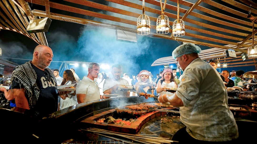 Chef serving buffet food at desert safari experience with guests in line.