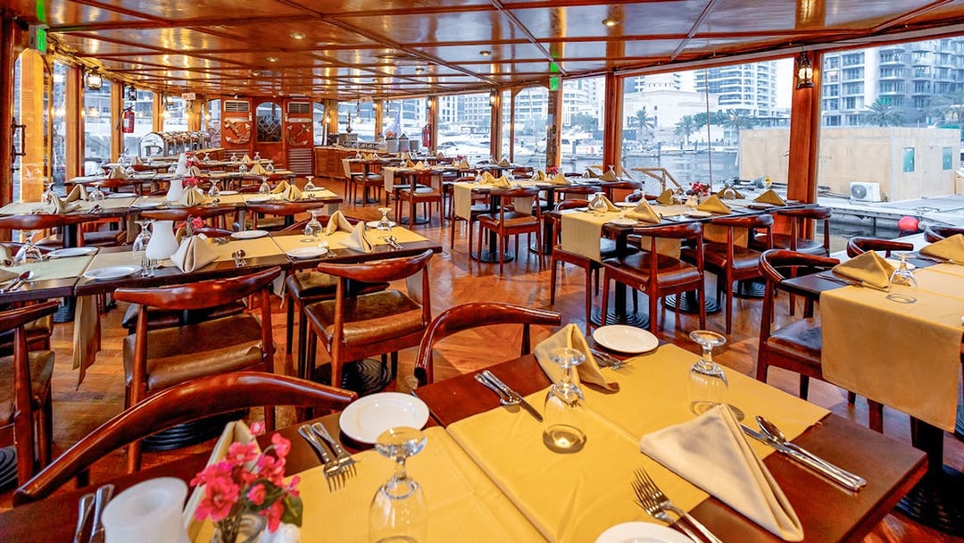 Dining setup on Alexandra Dhow Cruise in Dubai Marina with tables and city view.