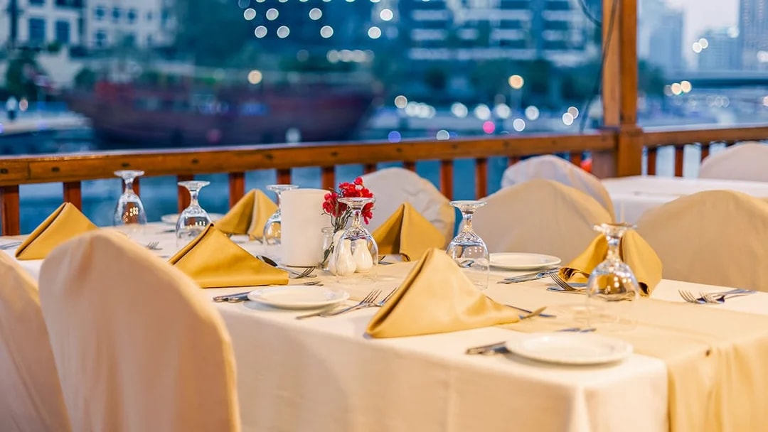 Dinner table setup on Alexandra Dhow Cruise, Dubai Marina, with city lights in the background.