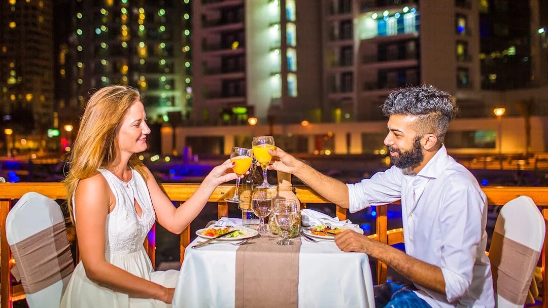 Couple toasting drinks during dinner on a dhow river cruise at night.
