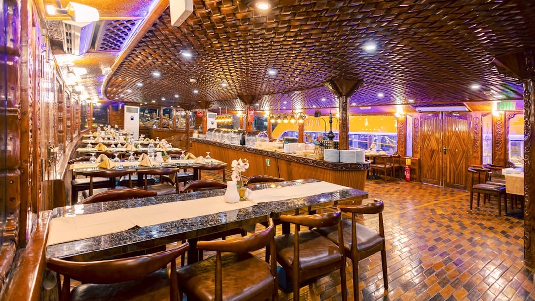 Interior dining area of Alexandra VIP Dhow Cruise with set tables and ornate wooden decor.