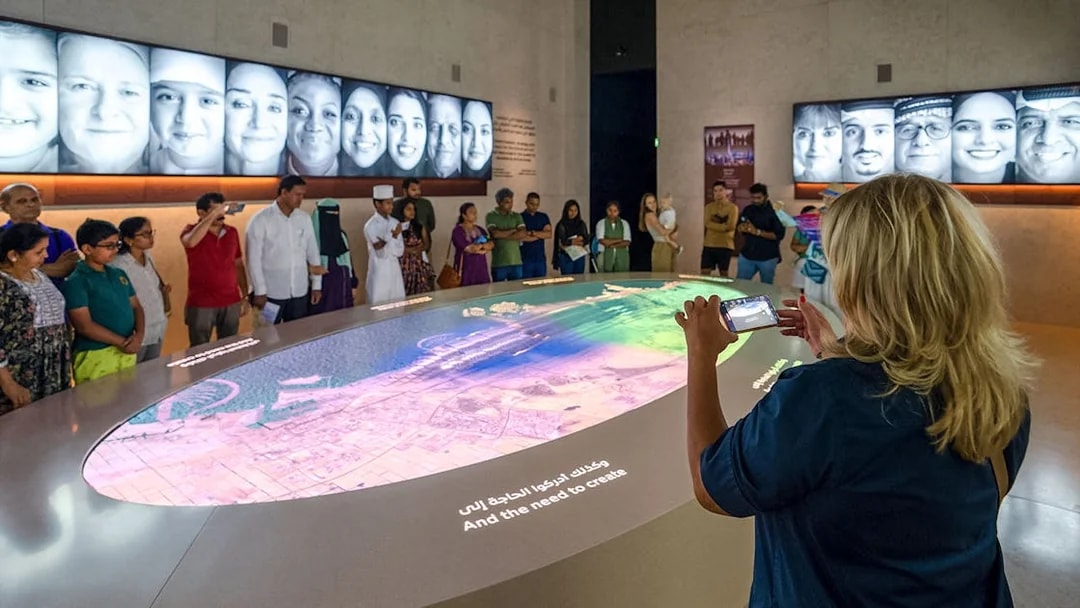 Tourist photographing interactive exhibit at Expo City Dubai with group observing.