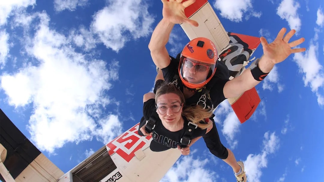 Tandem skydivers freefalling over Dubai's Palm Drop Zone with blue sky backdrop.