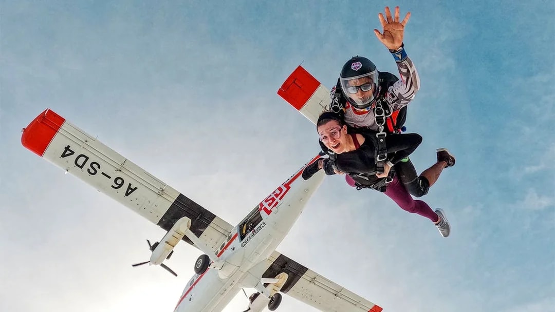 Skydivers tandem jumping from plane against clear sky.