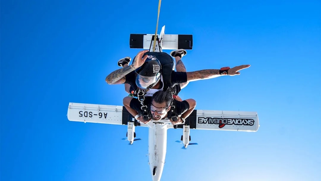 Skydiver tandem jumping from plane in Dubai against clear blue sky.