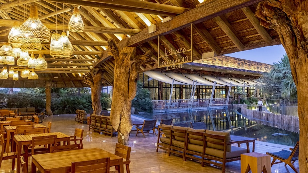 Outdoor dining area at Okavango Terrace with wooden tables and chairs under a thatched roof.
