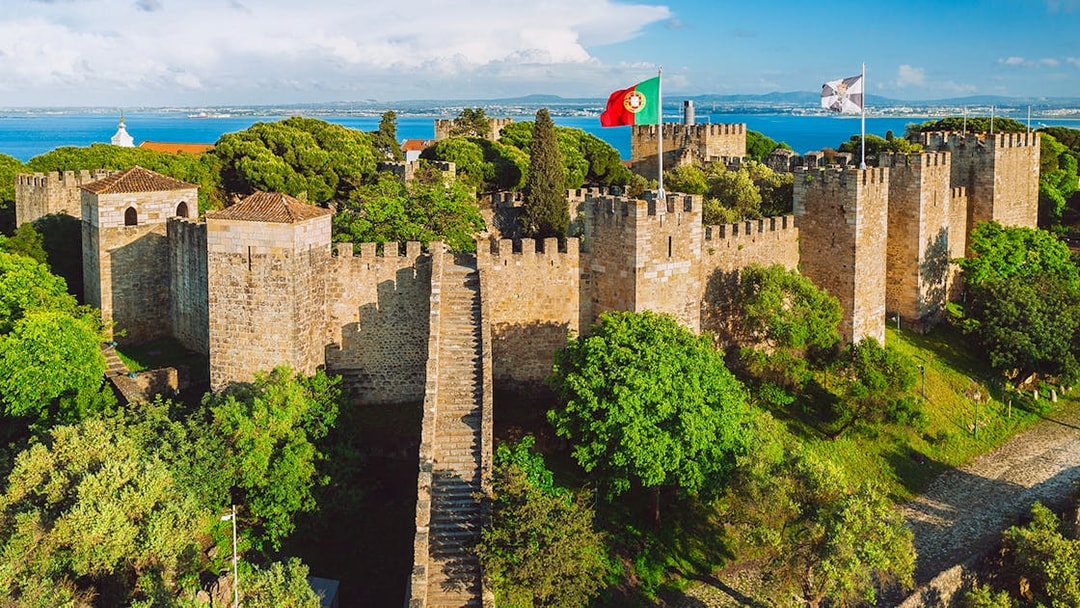 São Jorge Castle in Lisbon with stone walls, towers, and Portuguese flag.
