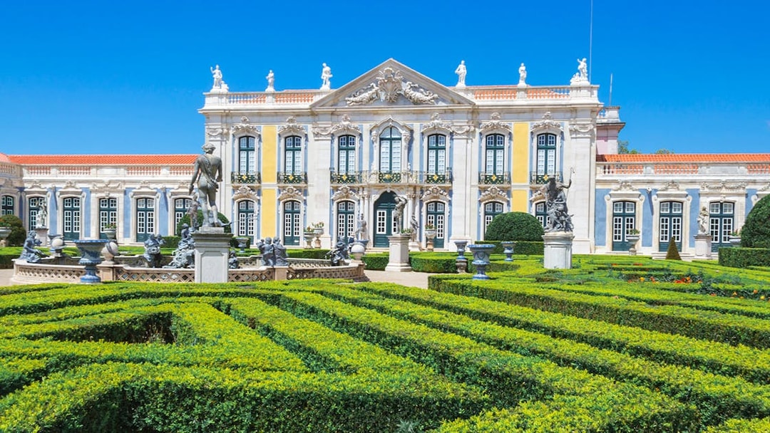 Queluz National Palace facade with manicured gardens and statues, Portugal.