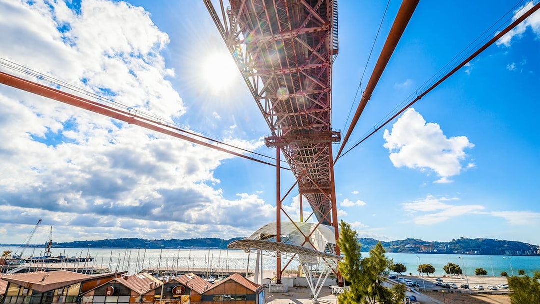 Underneath view of the Pilar 7 Bridge Experience in Lisbon, Portugal, with river and cityscape.