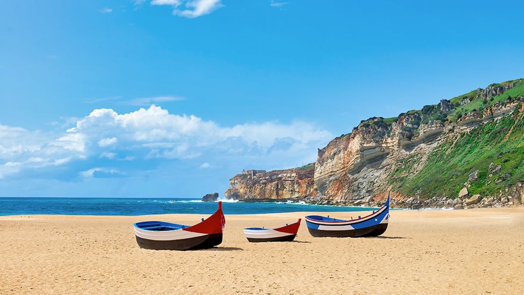 Traditional fishing boats on Nazaré beach with cliffs in the background, Portugal.