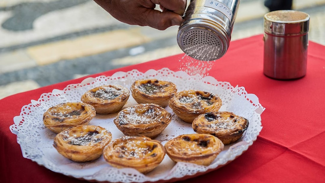 Pastéis de nata being sprinkled with sugar on a Lisbon walking tour.