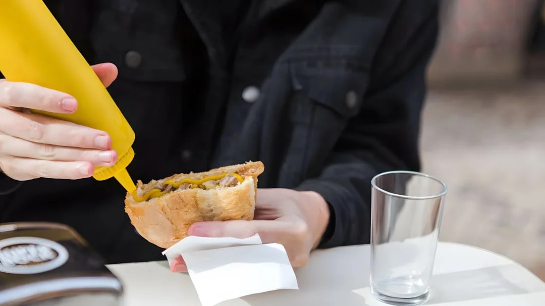 Person adding mustard to a Bifana sandwich in Lisbon.