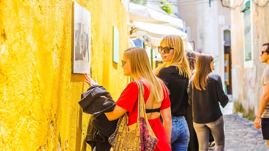Woman viewing Camilla Watson's portraits on a yellow wall in Lisbon.
