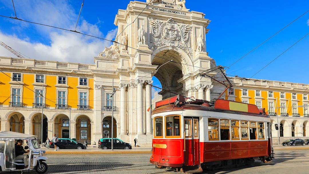 Lisbon tram passing by the Arco da Rua Augusta in a sunny city square.