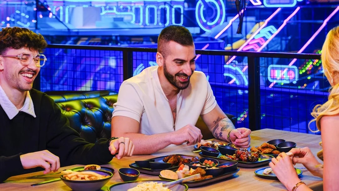 Group dining at Loco Bear entertainment hub with neon lights in the background.