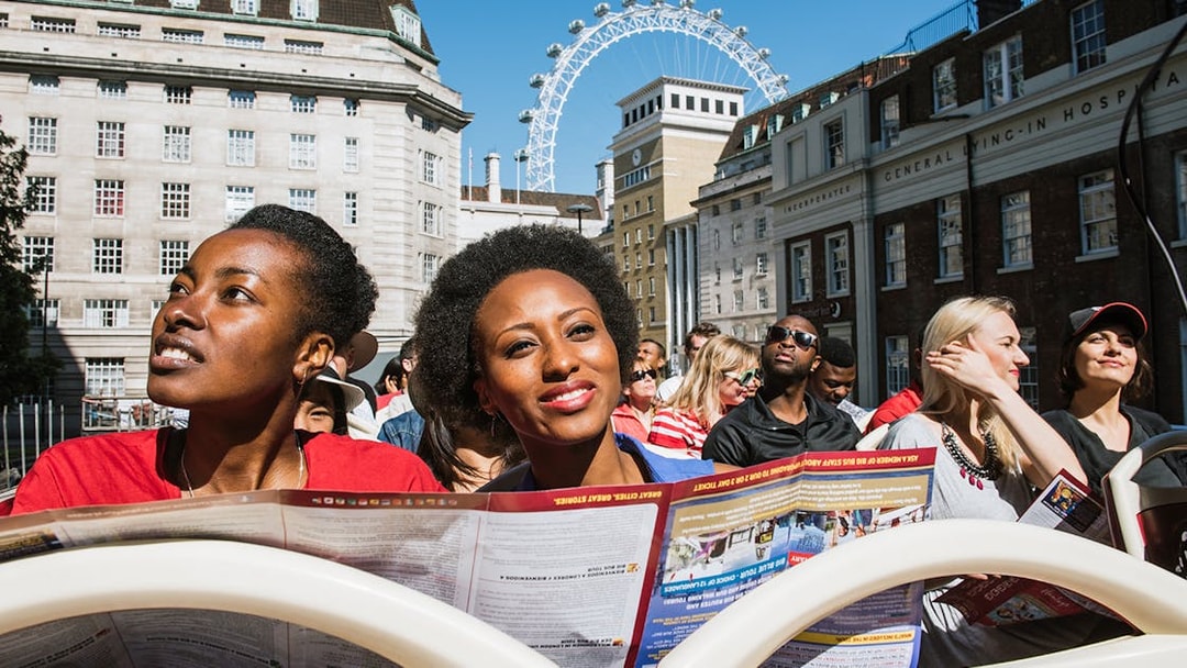 Tourists on BigBus London tour with London Eye in background.