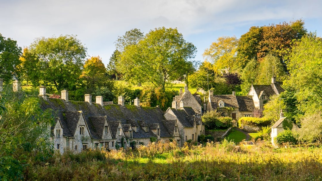Stone cottages in a Cotswolds village surrounded by lush greenery.
