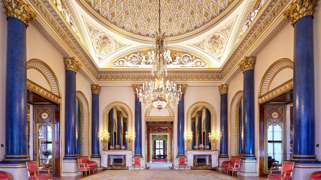 Music Room at Buckingham Palace with ornate ceiling, chandeliers, and blue columns.