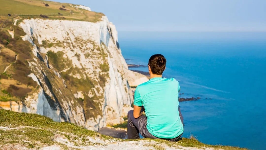 Person sitting on cliff overlooking the White Cliffs of Dover, England.