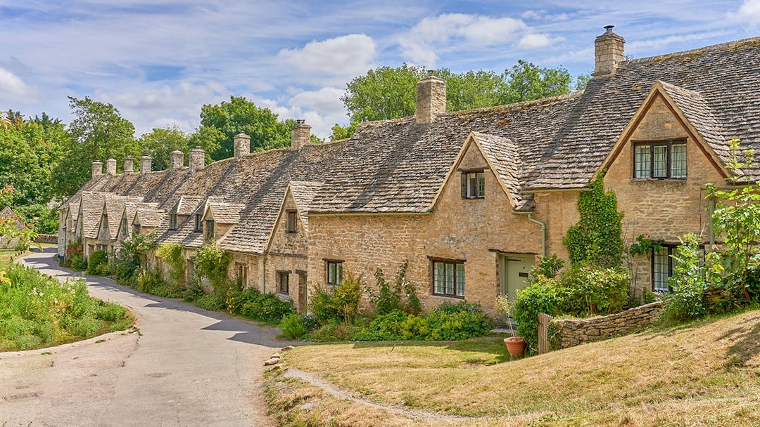Row of historic stone cottages in Bibury, Cotswolds, surrounded by greenery.