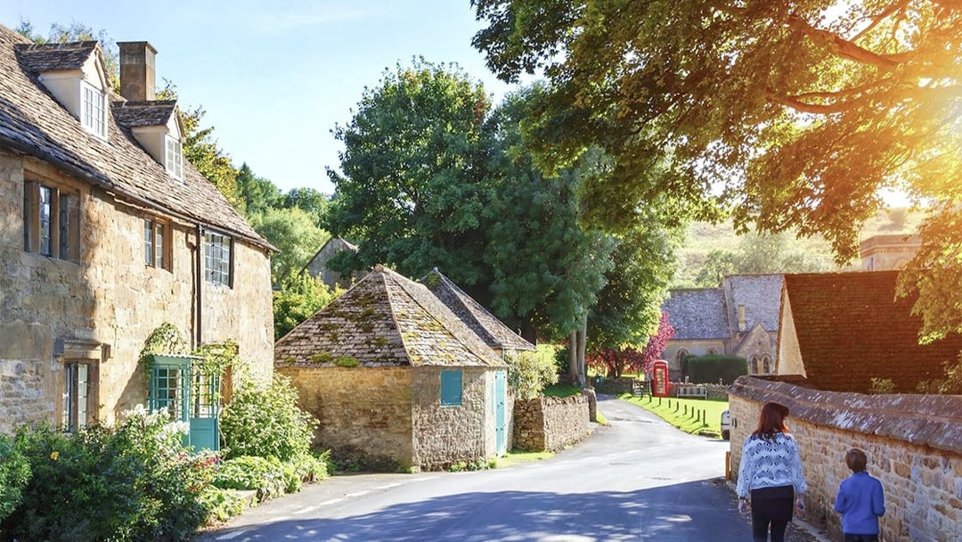 Cotswolds village street with stone cottages and lush greenery, part of small group tour.
