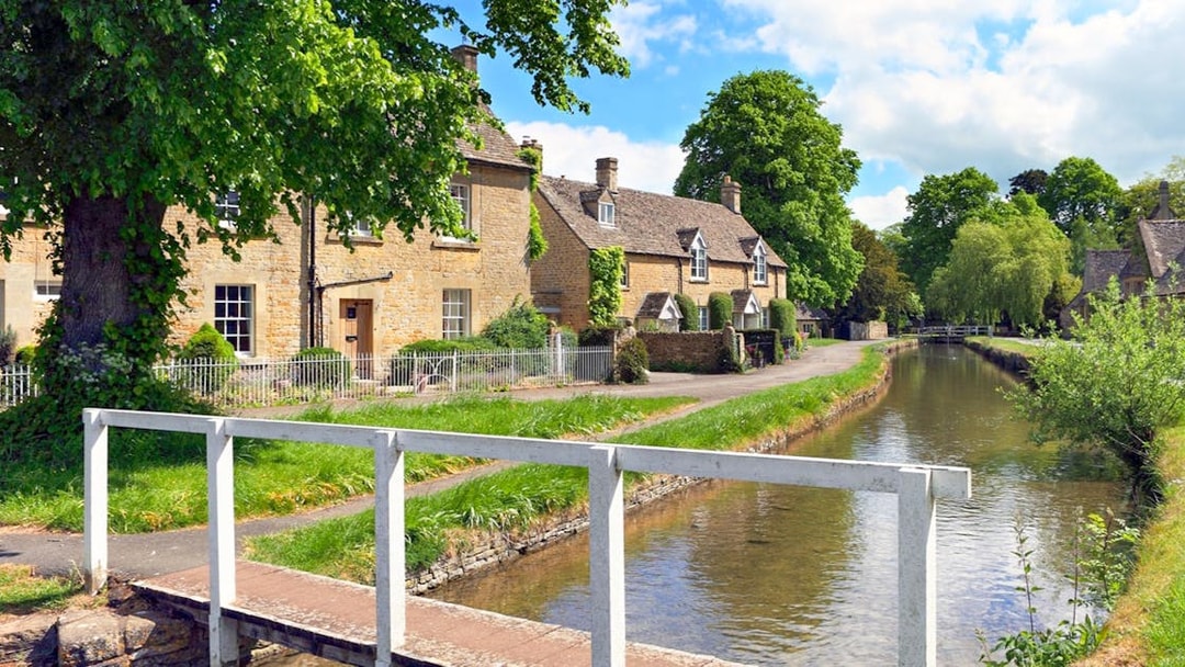 Cotswolds village houses by a canal with a footbridge, part of a small group tour.