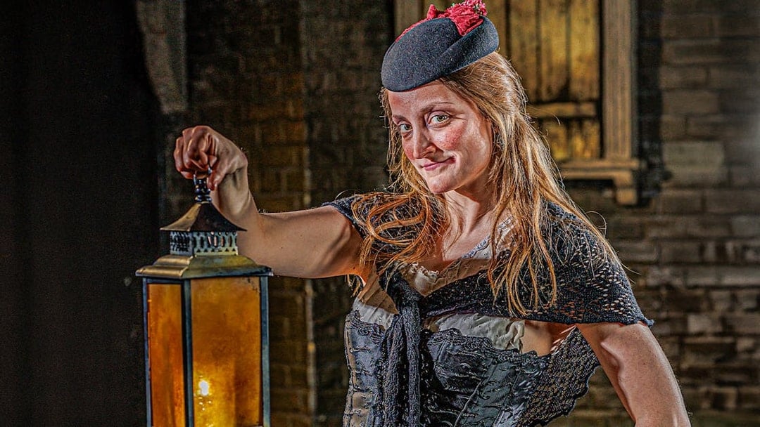 Guide in period costume holding lantern at London Dungeon.