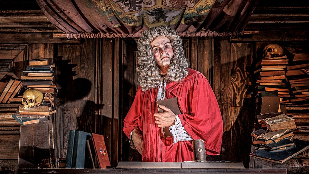 Judge in red robe at London Dungeon courtroom with books and skulls.