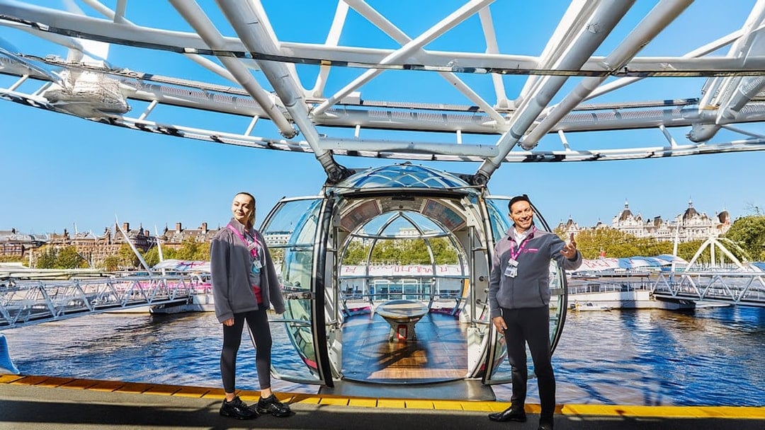 London Eye capsule entrance with staff welcoming visitors, view of Thames River.